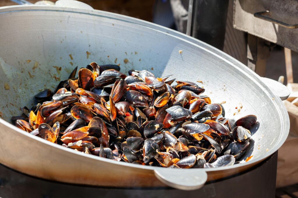 A close-up of freshly cooked mussels in a large wok, showcasing vibrant shellfish colors.