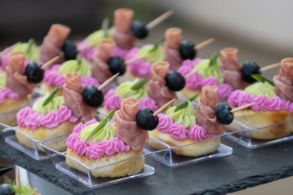 Delicious canapés with ham rolls, olives, and cream cheese frosting, perfect for events.