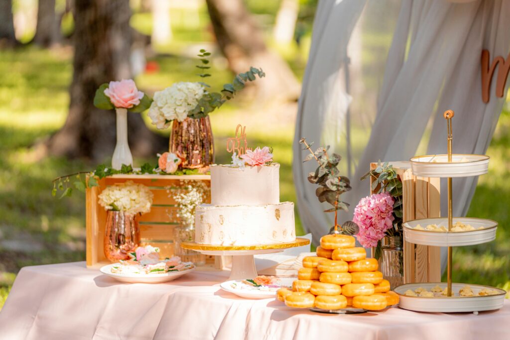 Beautiful outdoor dessert table with cake, donuts, and floral decor for a special event.