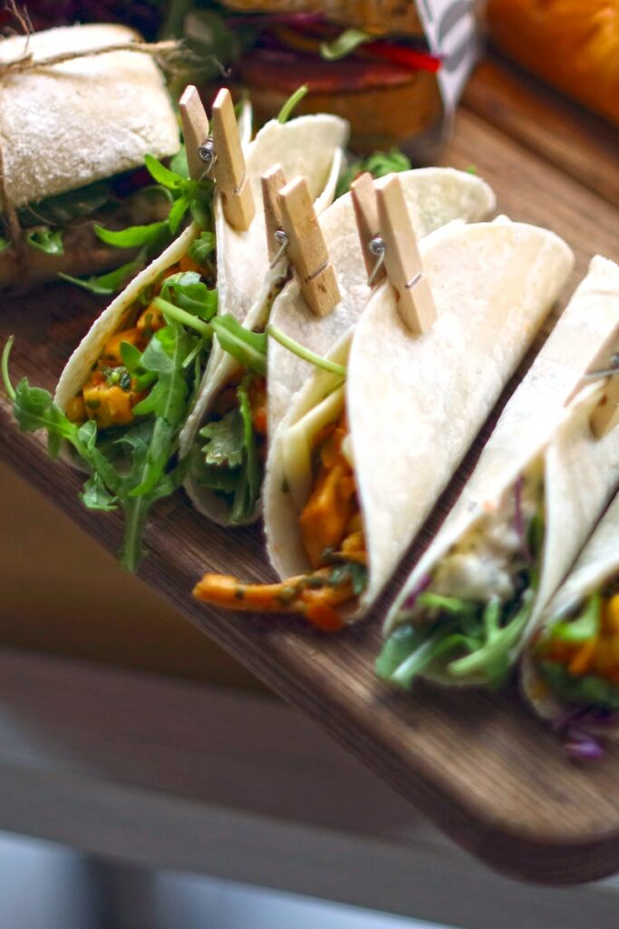Top view of assorted tacos and sandwiches on a wooden tray, perfect for catering or food photography.