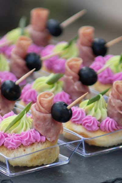 Delicious canapés with ham rolls, olives, and cream cheese frosting, perfect for events.