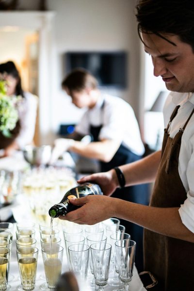 Waitstaff pouring champagne into glasses at a sophisticated indoor event.