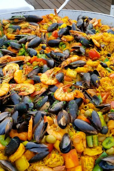 Close-up of a large pan of colorful seafood paella outdoors.