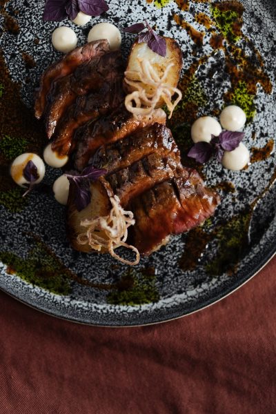 Flat lay of plate with exquisite arrangement of sliced roasted steak in garnish of cream and condiments
